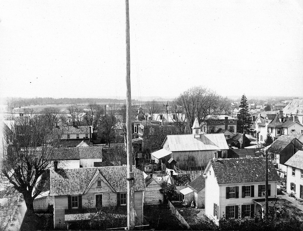 View from the school cupola over the front of the school, flagpole visible in foreground. Houses on Chestnut and Federal Streets are visible, but not the streets themselves. A portion of Wagamon's Pond is visible in the background.